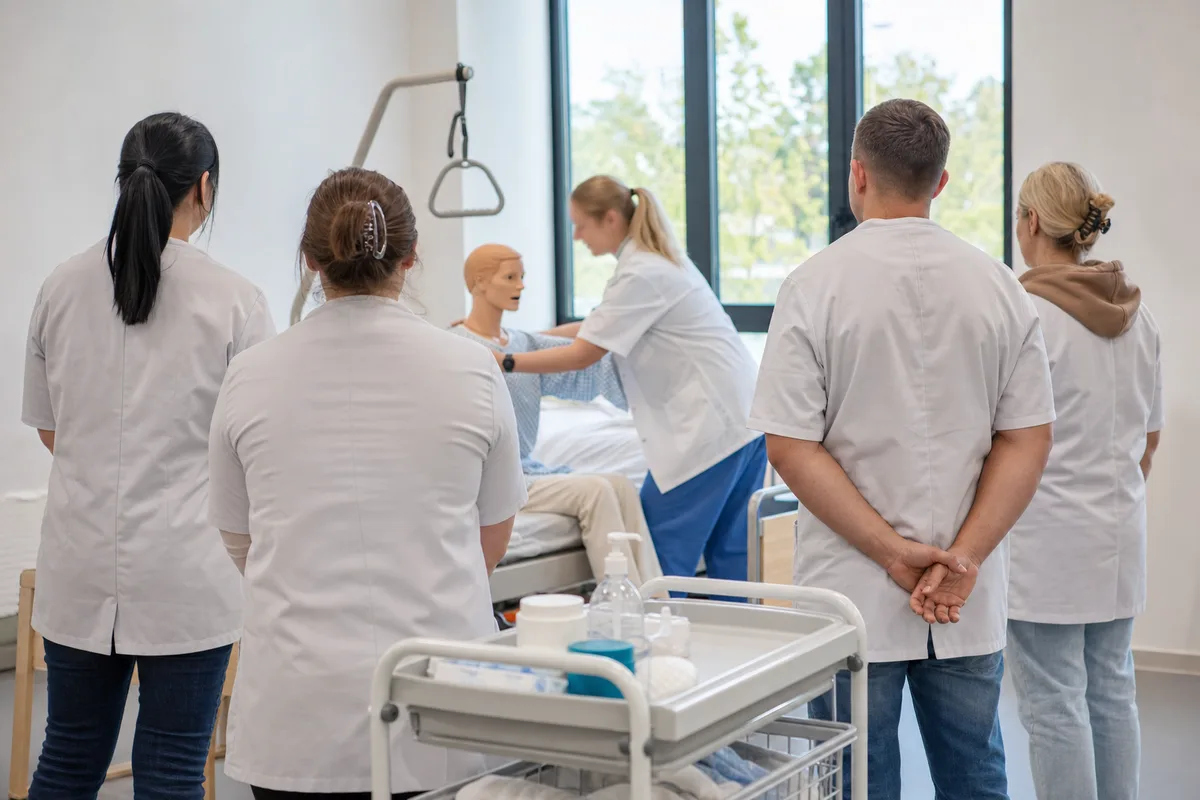 Formatrice guidant un petit groupe d’adultes en reconversion lors d’un atelier pratique de soin, mains au premier plan